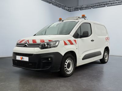 La camionnette blanche est garée dans une grande pièce ; elle porte une bande rouge et blanche sur le côté.