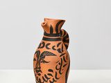 an orange and black vase sitting on top of a white table