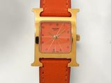 a gold watch with a red face on a tan leather strap