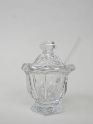 un bocal en verre contenant une cuillère, posé sur une surface blanche
