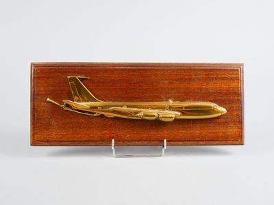 une image représentant une plaque en bois sur laquelle figure un avion doré