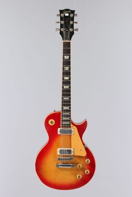une guitare électrique rouge et jaune accrochée à un mur blanc