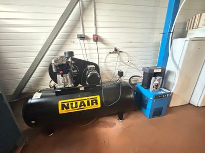 un compresseur noir posé dans un garage, à côté d'un réfrigérateur