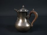 une cafetière ancienne en argent avec une poignée en bois, sur fond noir
