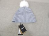 grey hat with white pom pom laying on a bed next to a tag