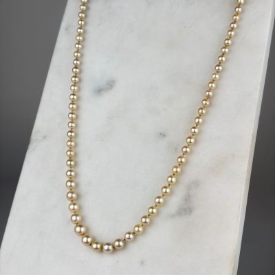 a gold beaded necklace on a marble stand
