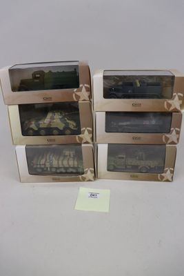 trois jouets représentant des véhicules militaires, présentés dans leurs boîtes respectives, posés sur une surface blanche