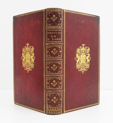 an old red book with gold trim sitting on top of a white table