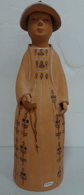 une statue en céramique représentant une femme coiffée d'un chapeau et tenant une canne