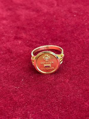 une bague en or ornée d'une couronne, posée sur un fond rouge