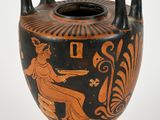 a black and orange vase on a stand on a white surface