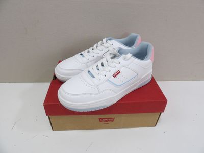des baskets blanches avec des bordures bleues, posées sur une boîte rouge