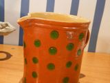 an orange pitcher with green dots on it sitting on a table