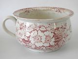 a red and white bowl with a handle on a white table
