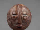 a wooden mask on a stand with a gray background