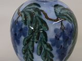 a blue vase with green leaves on it on a white surface