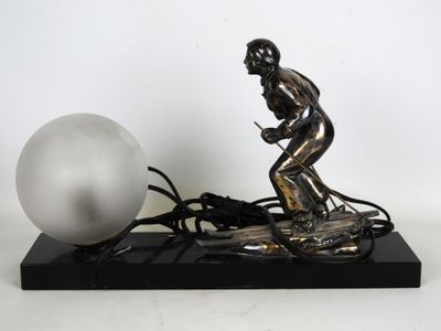 une statue en argent représentant un homme sur un skateboard, à côté d'une balle blanche
