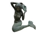 une statue représentant une sirène assise par terre, les mains sur la tête