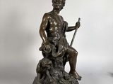 statue en bronze représentant un homme assis sur un rocher avec un chien