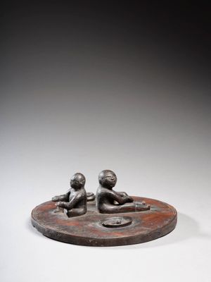 une sculpture en bronze représentant deux enfants assis sur un socle circulaire