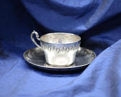 a silver cup and saucer sitting on a blue cloth