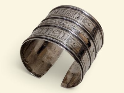 un gros plan d'un bracelet manchette en argent posé sur une surface blanche