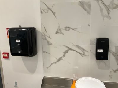 a toilet in a public restroom with a paper towel dispenser on the wall