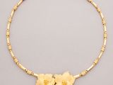 a gold necklace with flowers and beads on a gray background