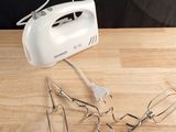a white hand mixer on a wooden table with other kitchen utensils