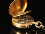 a gold pocket watch with a chain on a black surface