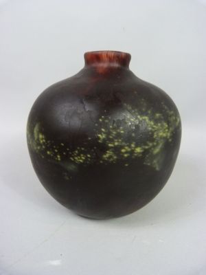 un vase noir parsemé de taches vertes, posé sur une surface blanche