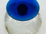 a glass vase with a blue lid sitting on a white surface