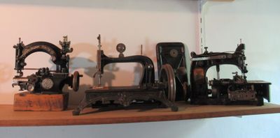 plusieurs machines à coudre anciennes sont posées sur une étagère dans une pièce