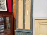 une armoire haute avec une porte vitrée, à côté d'une commode