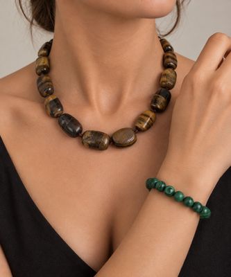 La femme porte une robe noire et un collier de perles vertes.