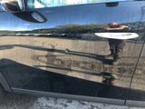a reflection of a man holding a surfboard on the side of a car