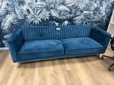 a blue velvet sofa in front of a wall with tropical wallpaper