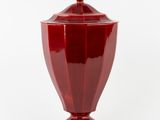 un vase rouge muni d'un couvercle, posé sur une surface blanche