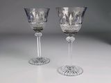 une paire de verres à pied en cristal posés sur une table blanche, sur fond gris