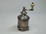 un moulin à café ancien en argent, surmonté d'une petite lampe jaune