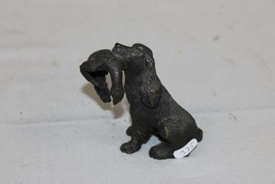 figurine représentant un chien noir tenant une médaille dans la gueule