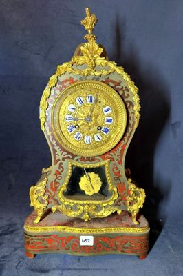 une horloge dorée et rouge posée sur un socle, sur fond bleu