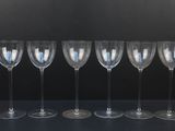 six empty wine glasses lined up in a row against a black background