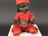 a black doll with a red hat sitting on a white cushion