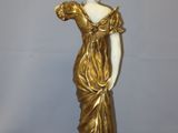 statue of a woman in a gold dress on a white surface