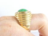 a person holding a gold ring with a green stone in it