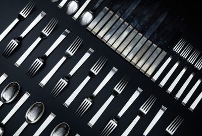 de nombreuses fourchettes et cuillères disposées sur une surface noire