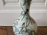 un vase blanc orné d'oiseaux, posé sur un plancher en bois