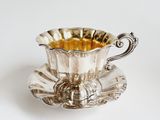 a silver cup and saucer sitting on a saucer