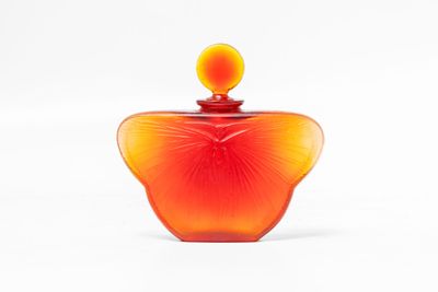 an orange glass perfume bottle with a yellow top on a white surface